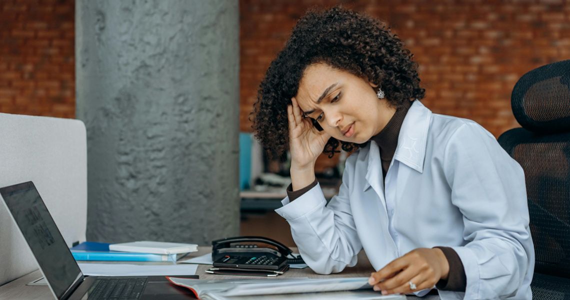 Female doctor sitting at a desk with her head in her hand looking tired