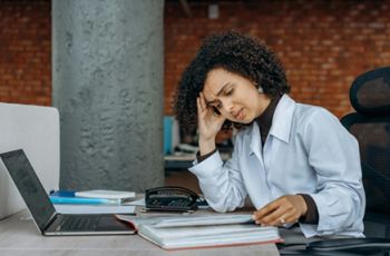 Female doctor sitting at a desk with her head in her hand looking tired